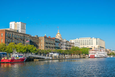 Buildings by river against clear blue sky