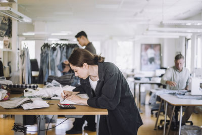 Young female fashion designer writing on package while working at workshop