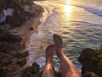 Low section of woman on mountain over sea during sunset