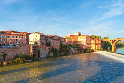 Buildings by river against blue sky