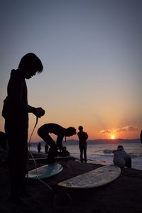 Silhouette people with surfboard on beach against sky during sunset