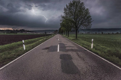 Road amidst green landscape against storm clouds