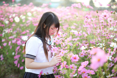 Young woman by pink flowers standing on field