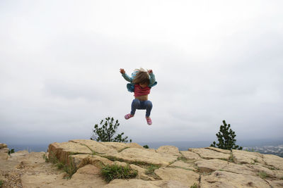 Full length of girl jumping on mountain cliff against sky at custer state park