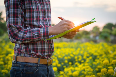 Midsection of man holding notepad while standing on agricultural field