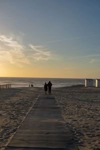 Silhouette people on beach against sky during sunset