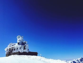 Low angle view of frozen built structure against clear blue sky during winter