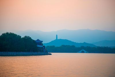 Sunset over beijing's summer palace, with layers of fog and silhouettes of hills, mountains, pagoda.