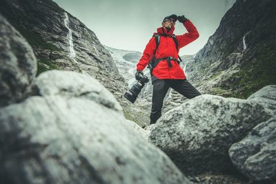 Hiker with digital camera standing on rock against mountain
