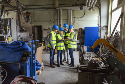 Full length of male and female workers using digital tablet in factory