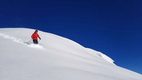 Low angle view of man skiing against clear blue sky