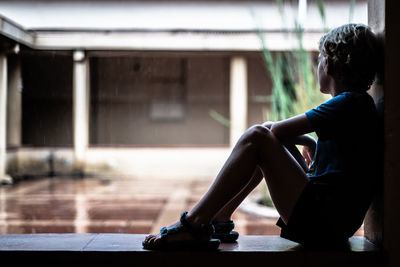 Side view of woman sitting on window