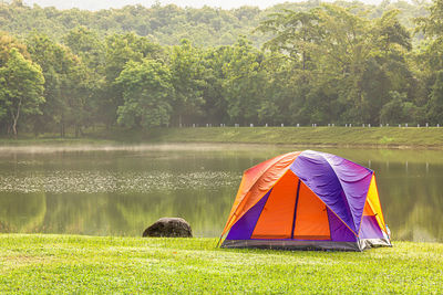 Scenic view of tent on grass by lake against trees