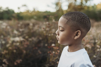 Side view of serious school-aged boy closing eyes in flower field