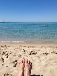 Low section of person at beach against clear sky