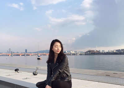 Young woman with eyes closed relaxing against sky at harbor