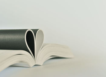 Close-up of open book with heart shape on table against white background