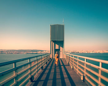 Woman walking on bridge over sea against sky during sunset