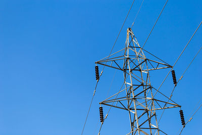 Low angle view of electricity pylon against clear blue sky