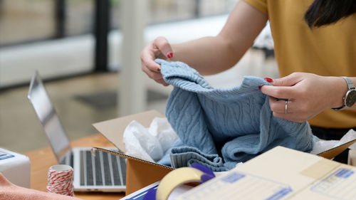 Online selling woman packing sweaters in boxes for delivery to customers, online selling.
