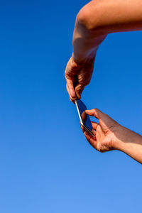Cropped hands of person taking a picture on a cellphone against blue sky