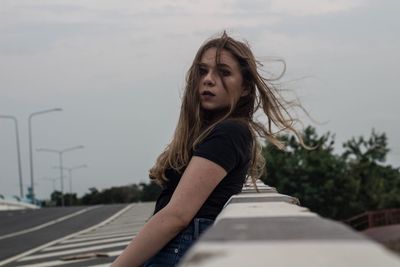 Side view of young woman standing on road against sky