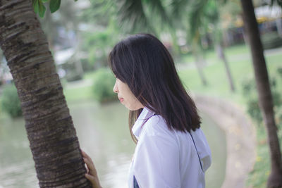 Woman standing by tree trunk in park