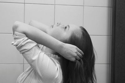 Side view of young woman with hand in hair while looking up against tiled wall