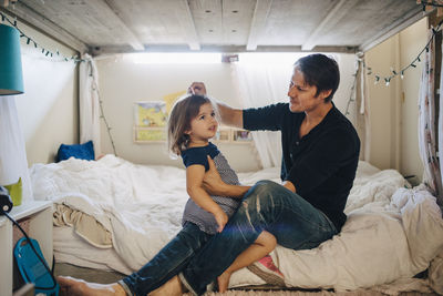 Father combing daughter's hair in bedroom