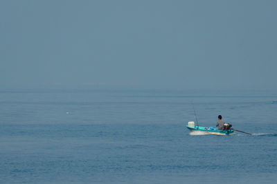 Man rowing boat in sea against sky