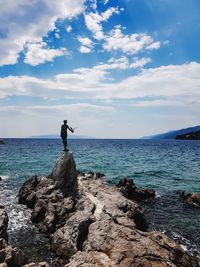 Man standing on rock by sea against sky