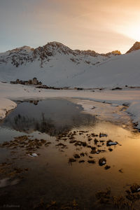 Scenic view of lake by snowcapped mountains against sky during sunset