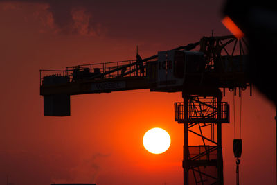 Low angle view of silhouette crane against orange sky