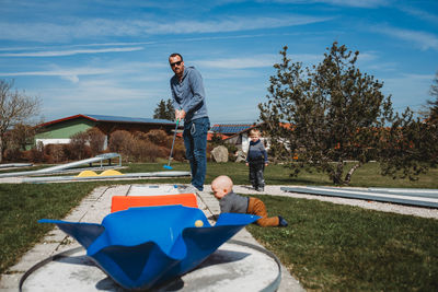 Father and son playing mini golf in farm on sunny day