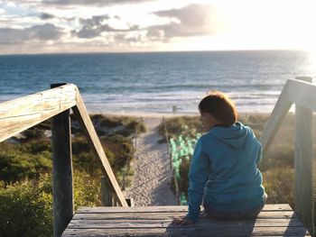 Rear view of man sitting on railing against sea