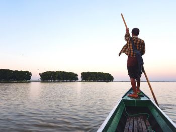 Rear view of man standing on boat at lake