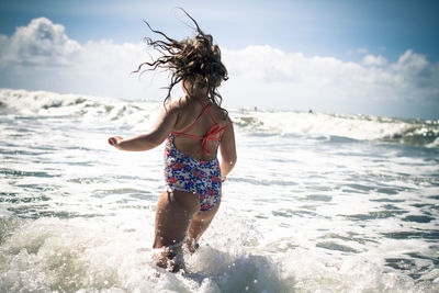 Rear view of girl running in water against sky during sunny day