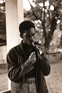 Man smoking cigarette while standing against trees