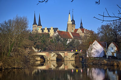 Arch bridge over river by buildings against clear sky