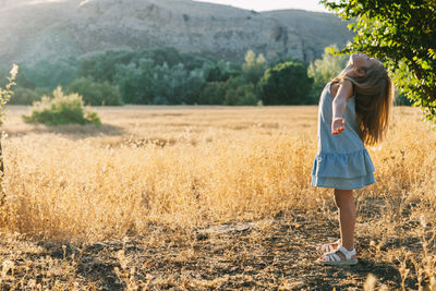 Side view of girl with arms outstretched standing on grassy field against mountain