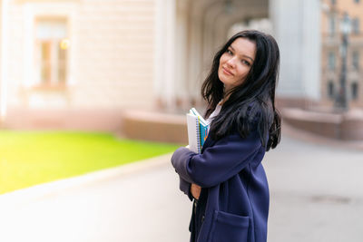 Side view portrait of young woman holding books outside university
