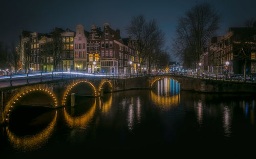 Illuminated bridge over river in city at night