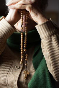 Midsection of senior woman holding wooden rosary beads with cross