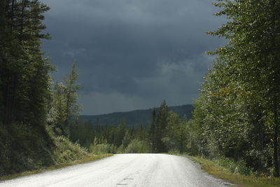 Empty road amidst trees against sky