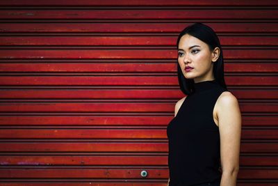 Woman looking away while standing against red wall