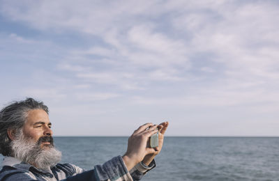 Happy bearded man taking selfie or photo with smart phone standing on the beach person