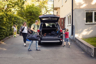 Man and woman loading luggage in trunk while boy charging electric car