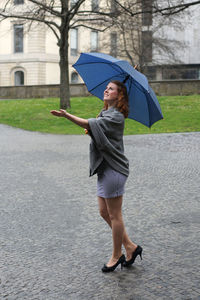 Smiling woman with umbrella standing on footpath at park