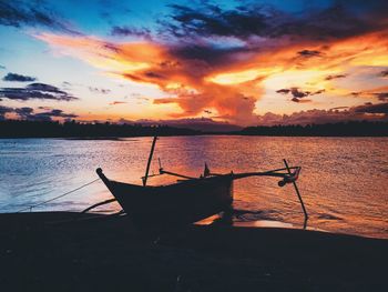 Silhouette boat moored on beach against sky during sunset