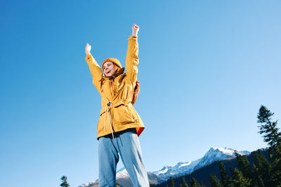 Rear view of woman with arms raised against clear blue sky